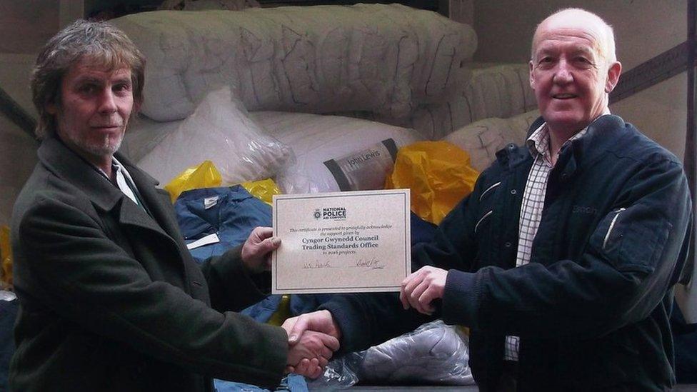 John Eden Jones from Gwynedd Council's Trading Standards Service handing over the counterfeit clothing to David Scott from the National Police Aid Convoy charity