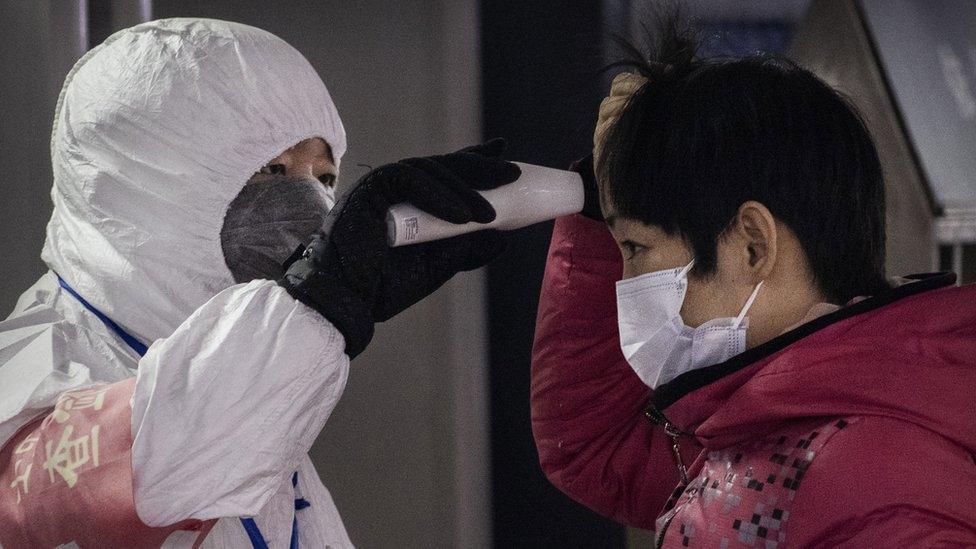 man-in-white-suit-takes-temperature-of-woman-wearing-mask