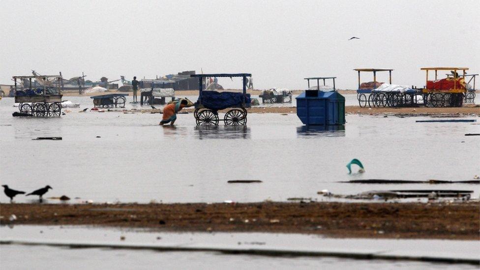 An Indian woman pushes a cart on the waterlogged Marina Beach after heavy rainfall in Chennai, India, Friday, Nov. 13, 2015.