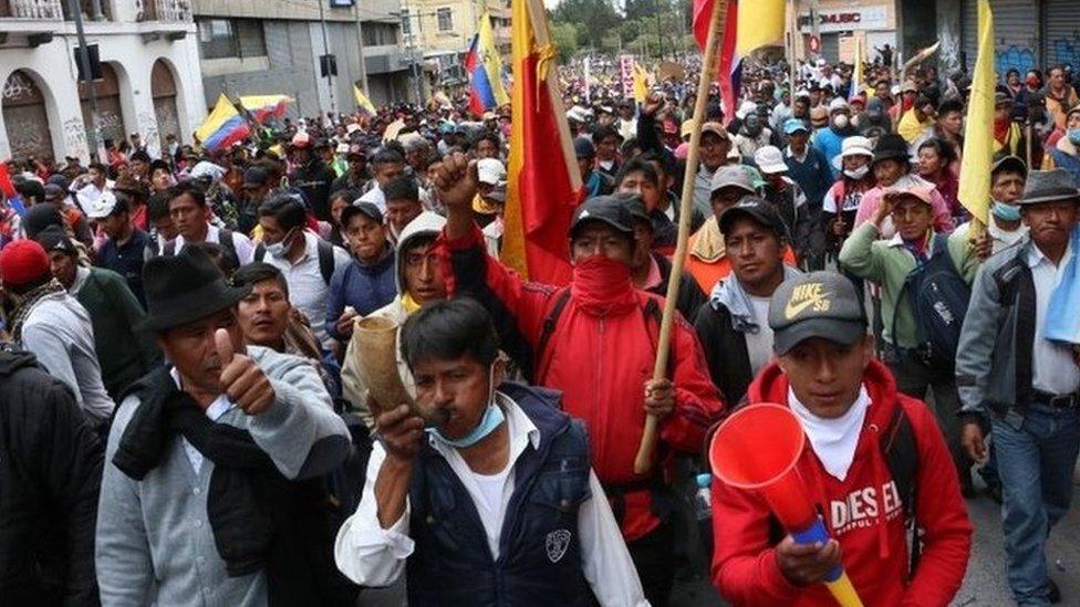 People holding flags and horns as they march through the streets