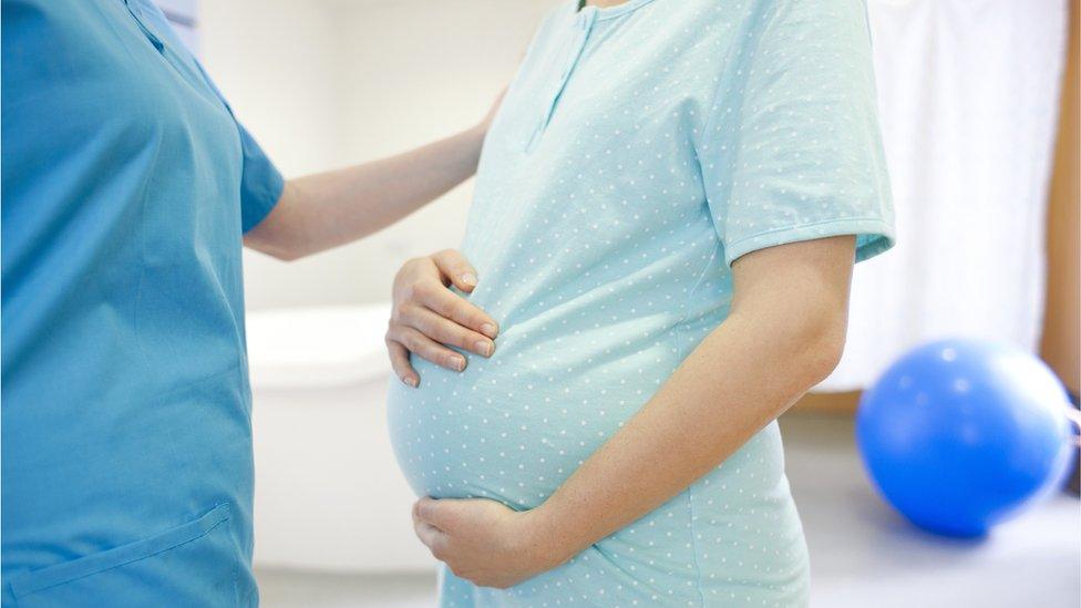 Pregnant woman during early labour at a birthing centre a midwife has her hand on her shoulder