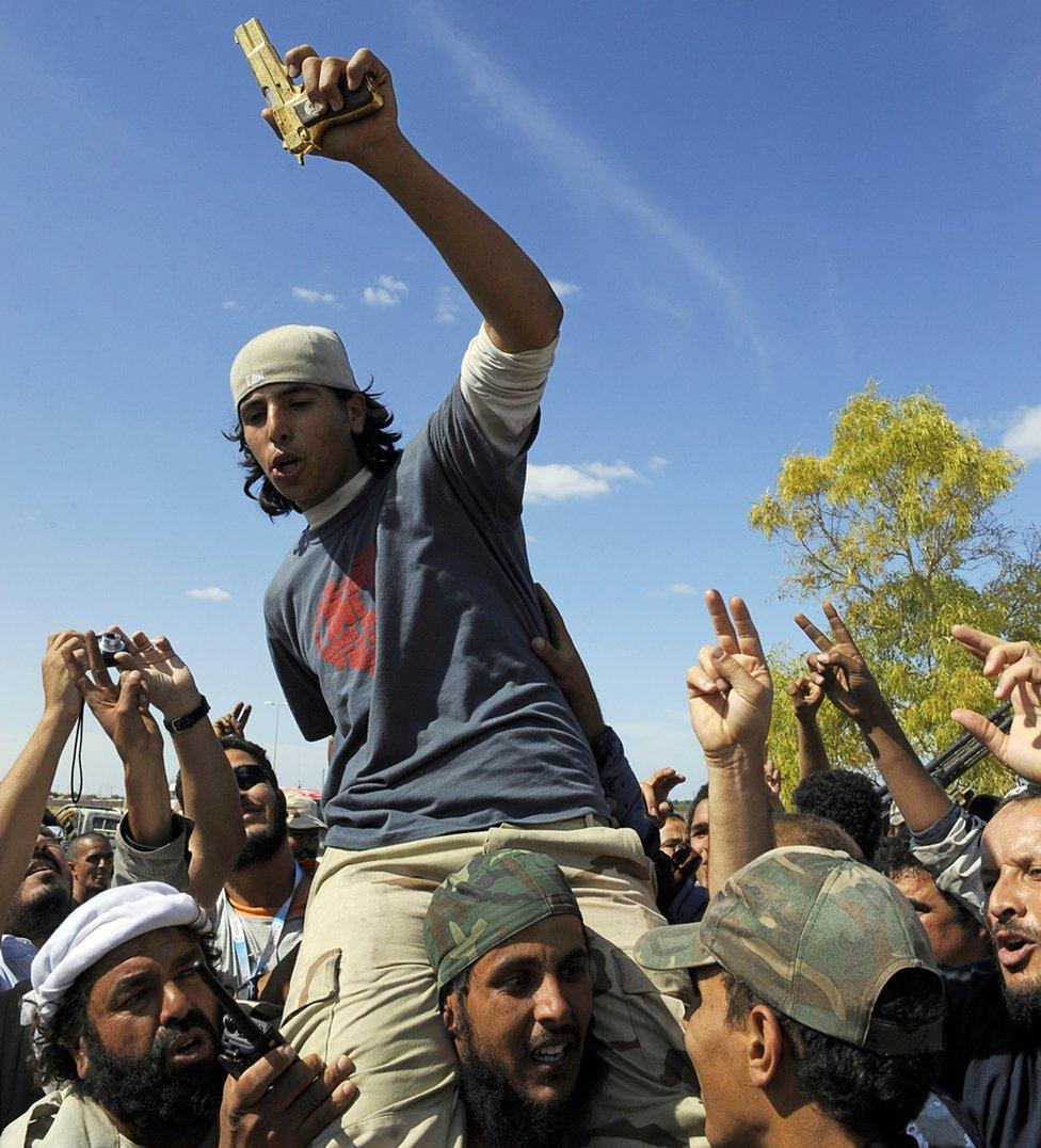 Man in blue T-shirt and baseball cap holding golden gun