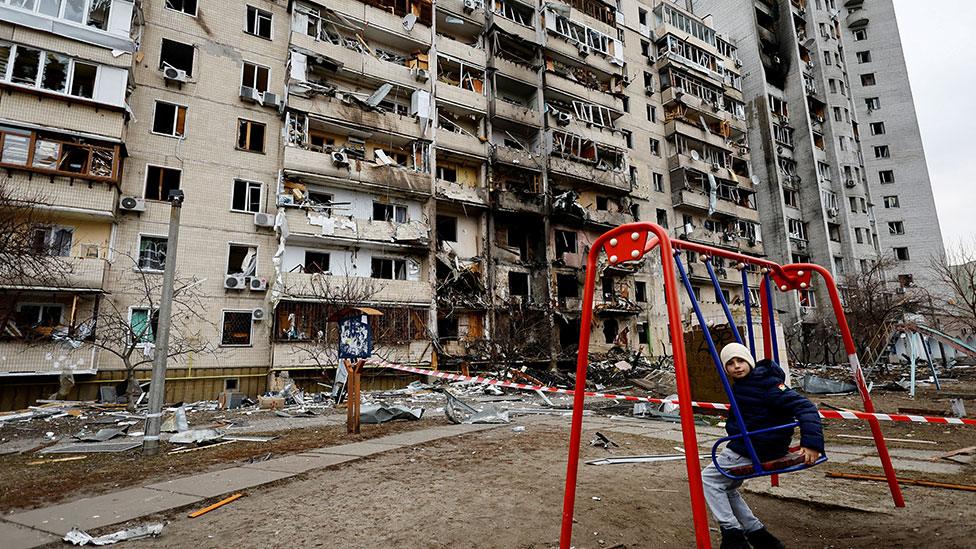 A child on a swing outside a damaged residential building in Kyiv