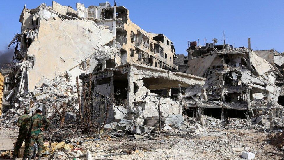 Syrian government forces stand in front of destroyed buildings in the Hajar al-Aswad district of Damascus (21 May 2018)