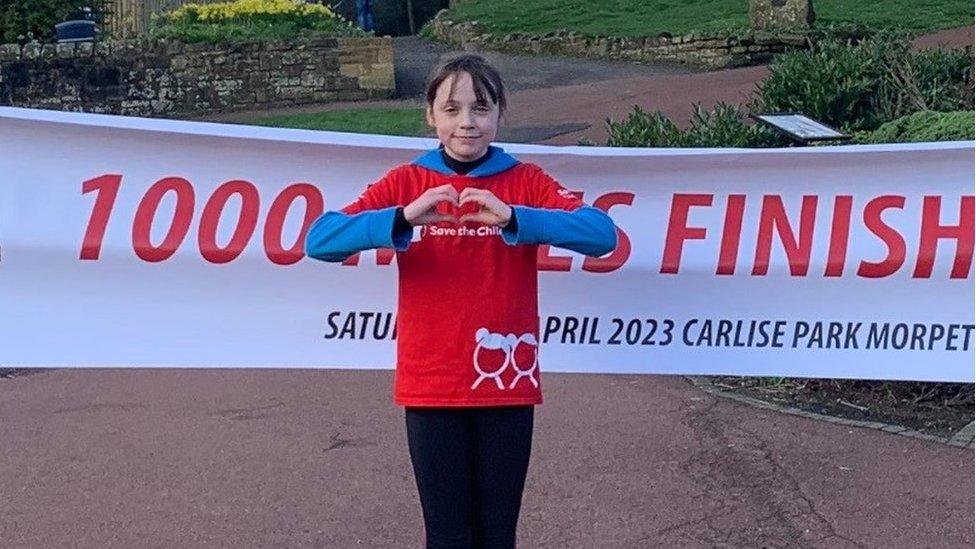 Sienna in front of the finish line, holding her hands in a heart symbol