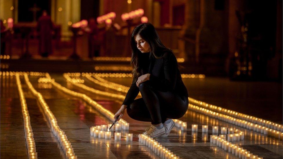 Holly Wilson, whose grandmother Ada Wilson passed away during the pandemic, lights a candle in Belfast Cathedral - the floor of the cathedral is covered in the lights