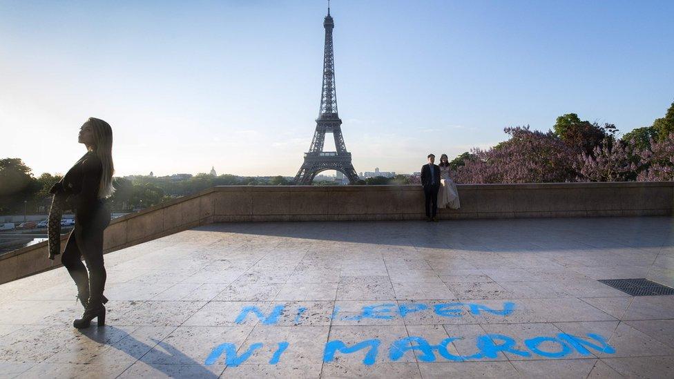 People pose for pictures in front of the Eiffel Tower at the Trocadero plaza, where a graffiti on the ground, referring to the second round of the presidential election in France, reads "Neither Le Pen, nor Macron"