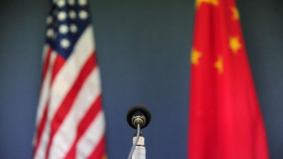 photograph shows a united states flag and a chinese flag in the background behind a microphone