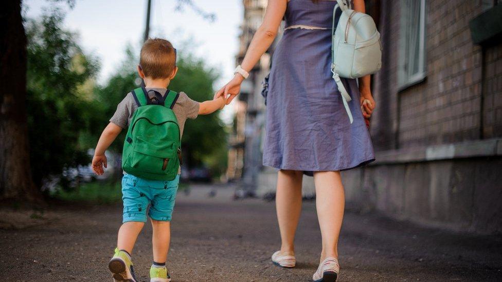 Woman and boy walk away holding hands