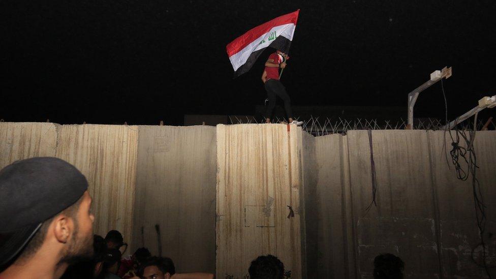 Iraqi protester carries an Iraqi flag on the wall around the Iranian consulate in the holy city of Karbala (3 November 2019)