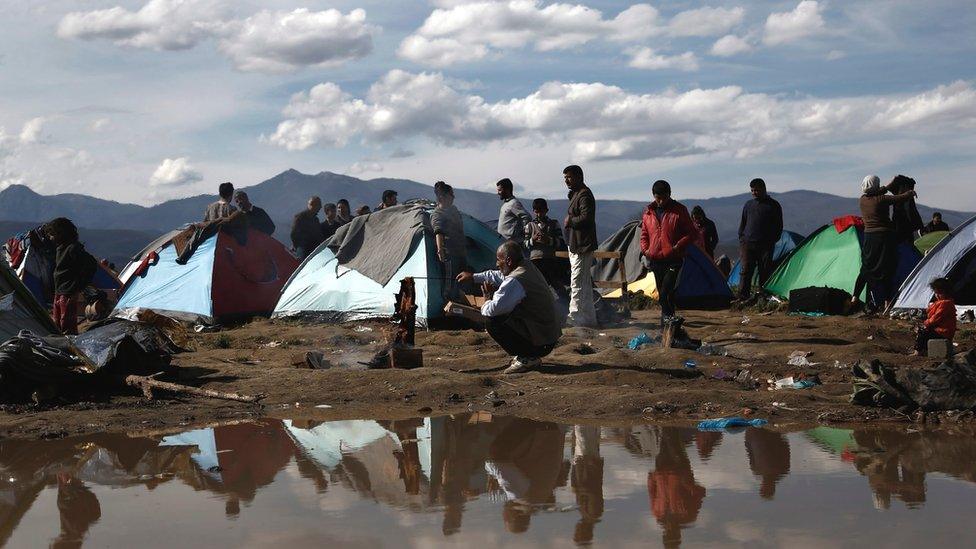 Refugees and migrants stand in front of their tents, following an overnight storm at the refugee camp of Idomeni, near the Greek border with Macedonia, northern Greece, 8 March 2016