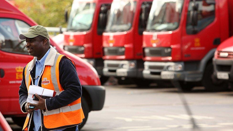 A Royal Mail employee walks past vans