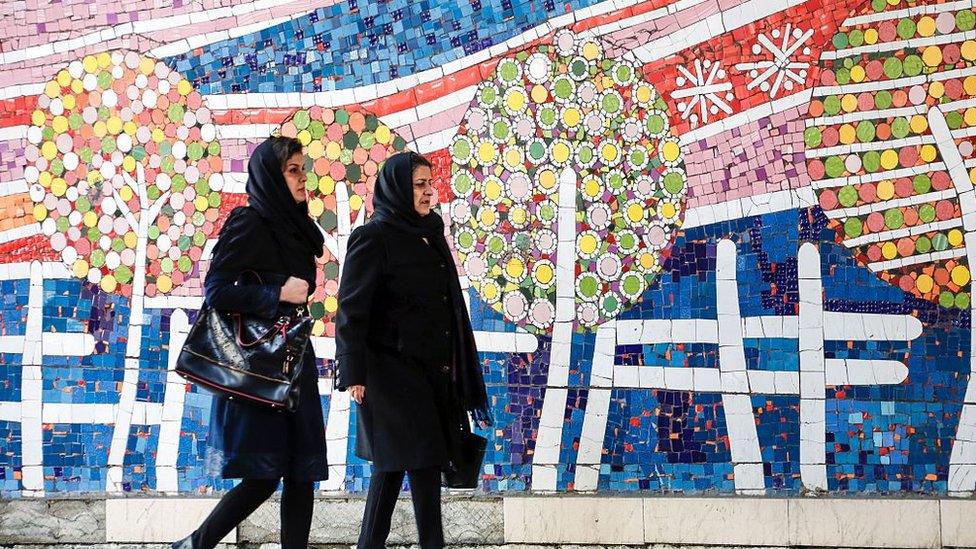 Iranian women walk past mural in Tehran (file photo)