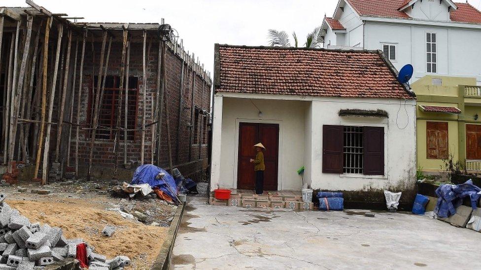 A Vietnamese woman stands near an under-construction house in Yen Thanh district