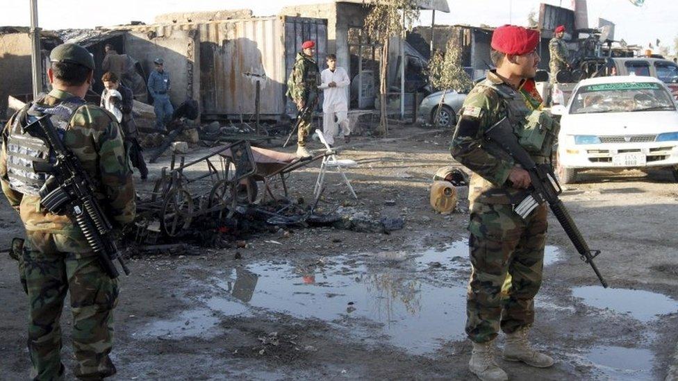 Afghan National Army (ANA) soldiers stand guard in front of a shop burned during the Taliban attack on Kandahar Airport (09 December 2015)