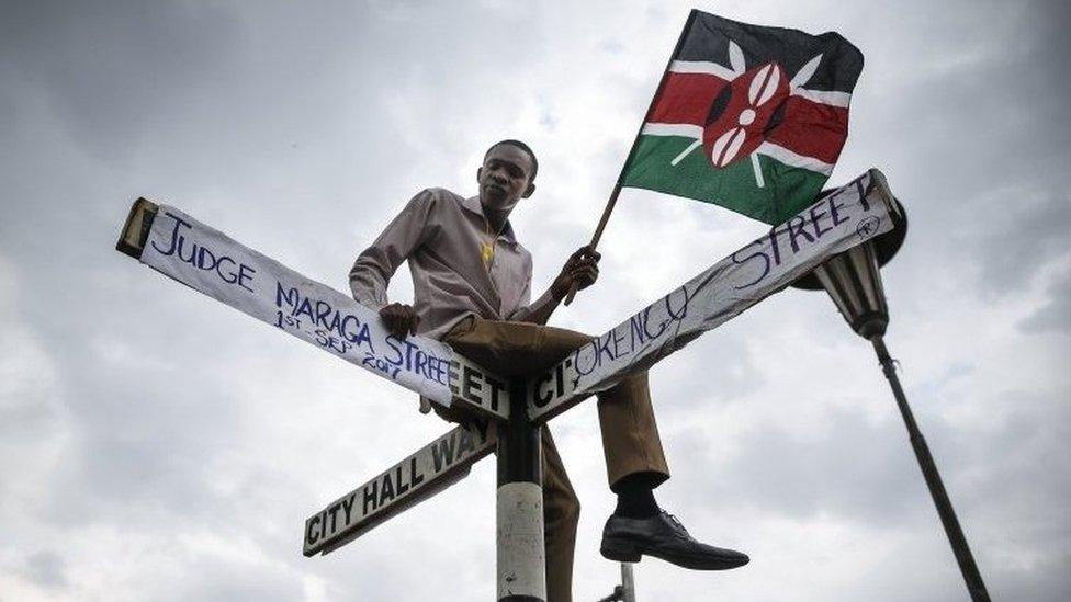 A supporter of The National Super Alliance (Nasa) opposition coalition and its presidential candidate Raila Odinga sits on top of a street sign post that has been relabeled "Judge Maraga Street", referring to Chief Justice David Maraga,