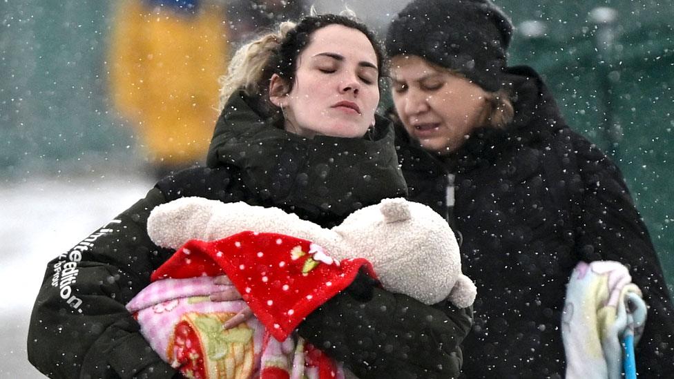 A woman carries an infant as they cross the border into Poland from Ukraine