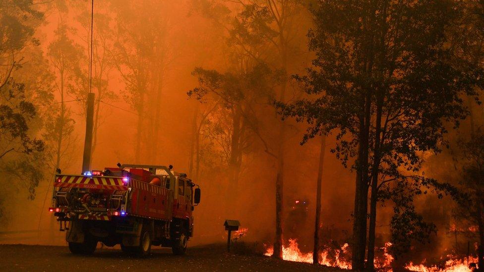 A fire truck near a raging fire in Werombi, south-west of Sydney, against a bright orange sky