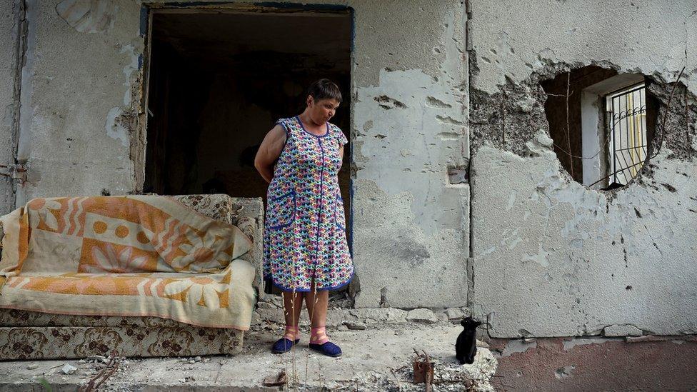 Woman in front of wall with a hole blasted in it