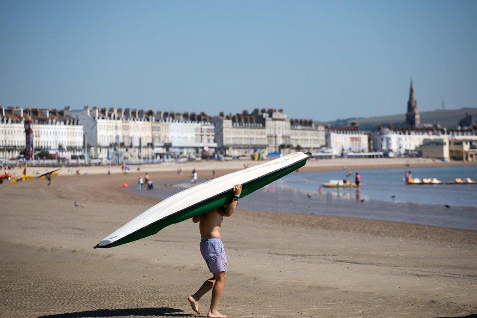 A man carries a paddle board down to the sea at Weymouth seafront in Dorset, England