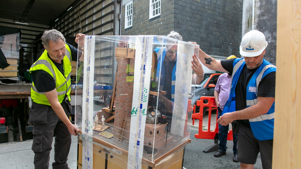 Men carrying miniature engine collection into museum