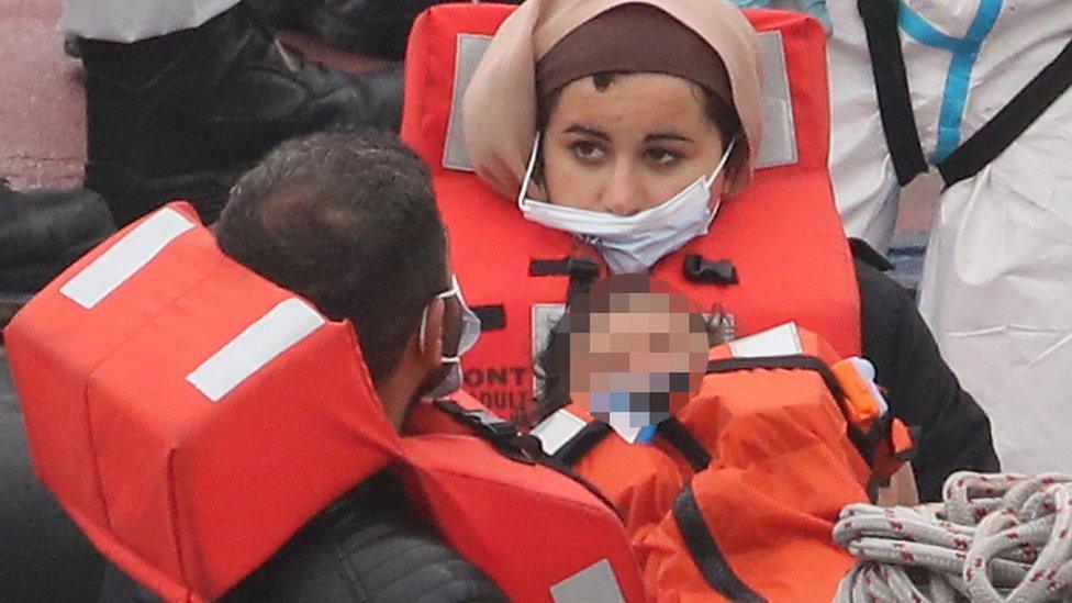 A man carries a young child as a group of migrants are brought into Dover on a Border Force vessel on Sunday