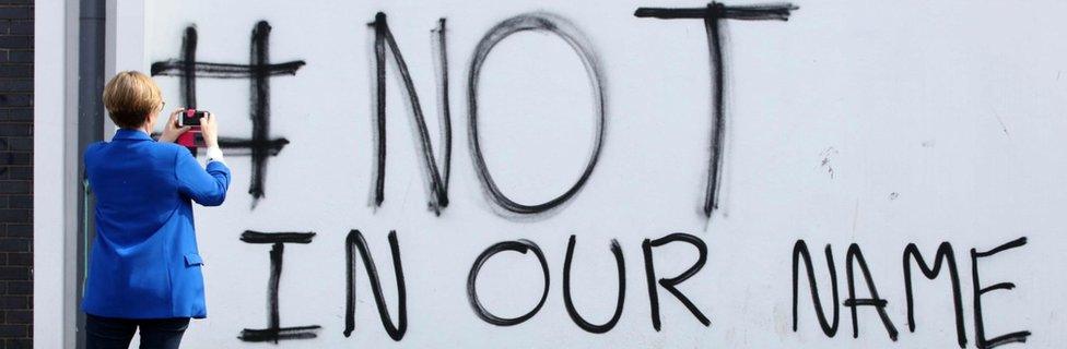 A pedestrian takes a picture of new graffiti that reads "#not in our name" in the Creggan area of Derry (Londonderry) in Northern Ireland, close to the scene where journalist Lyra McKee was fatally shot