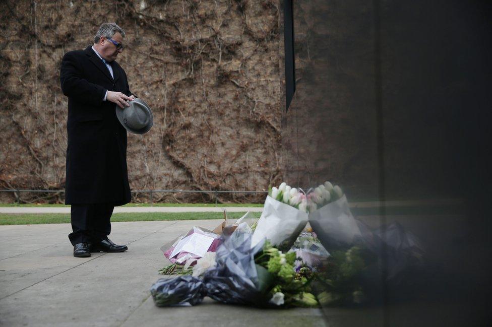 A man pauses in front of floral tributes