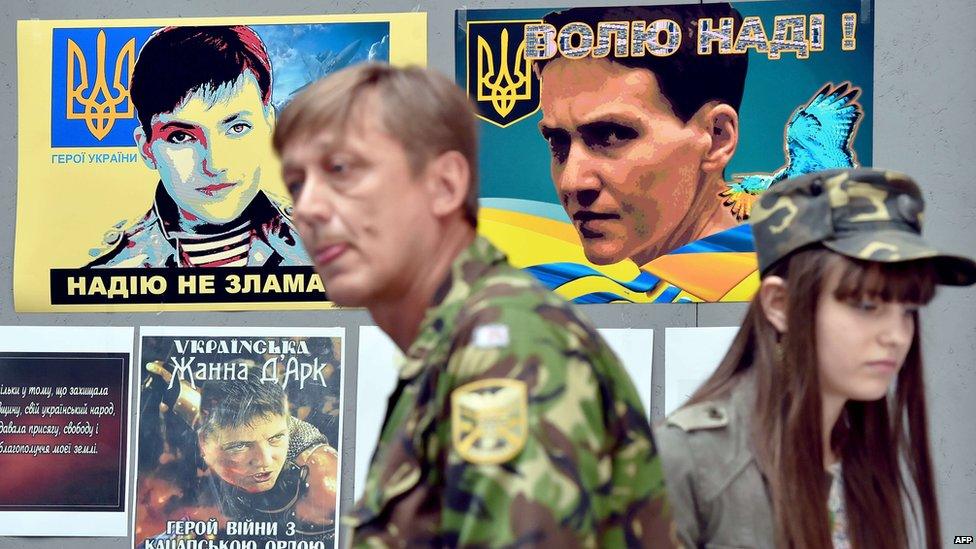 A Ukrainian serviceman and a girl wearing military fatigues walk in front of placards bearing pictures of Nadia Savchenko in Kiev (19 June 2015)