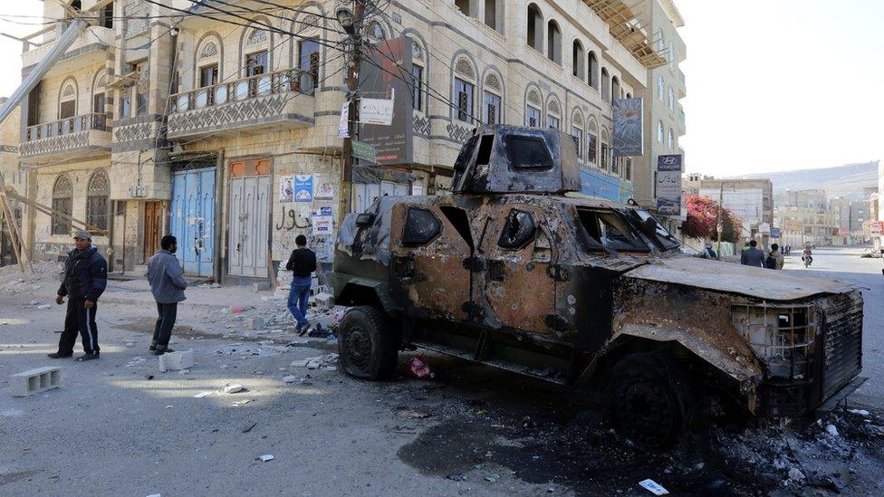 Yemenis walk past a destroyed armoured vehicle in a street leading to the residence of Yemen's ex-president Ali Abdullah Saleh in Sanaa (5 December 2017)