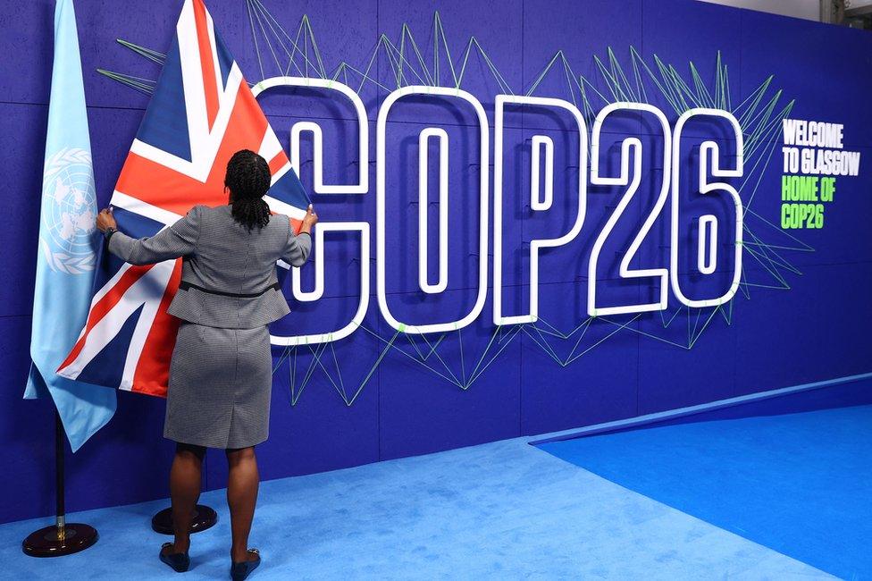 A summit organiser adjusts flags before the arrival of leaders for the COP26 UN Climate Summit in Glasgow on 1 November 2021