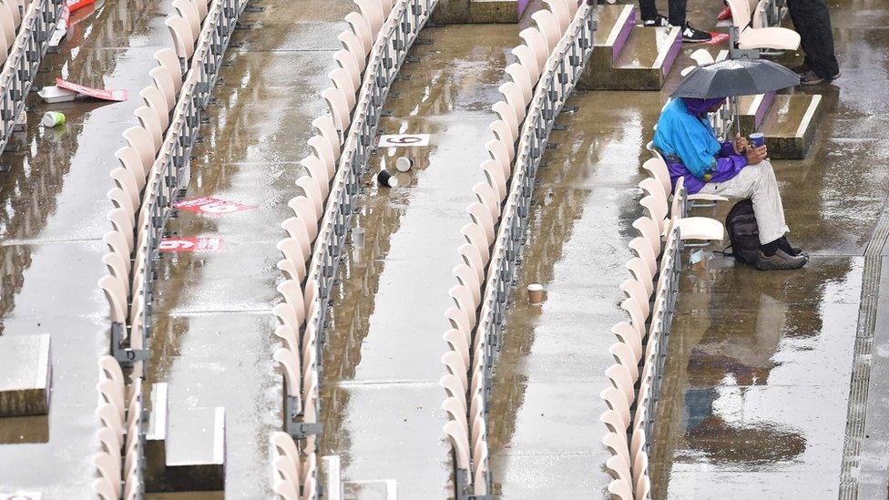 A spectator sits under an umbrella at a rain-soaked Rose Bowl