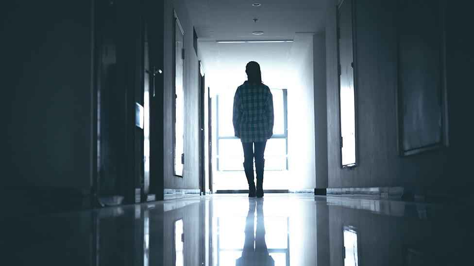 Silhouette of young woman in what looks like a dark hospital ward