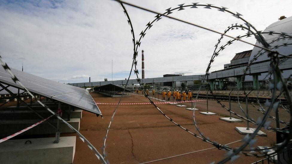 Solar panels are seen through barbed wire in front of the New Safe Confinement arch at a newly-built solar power plant in Chernobyl, Ukraine October 5, 2018.