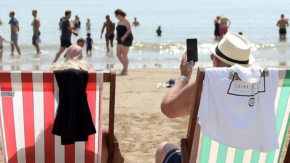 Two people sit on beach deckchairs, facing the sea