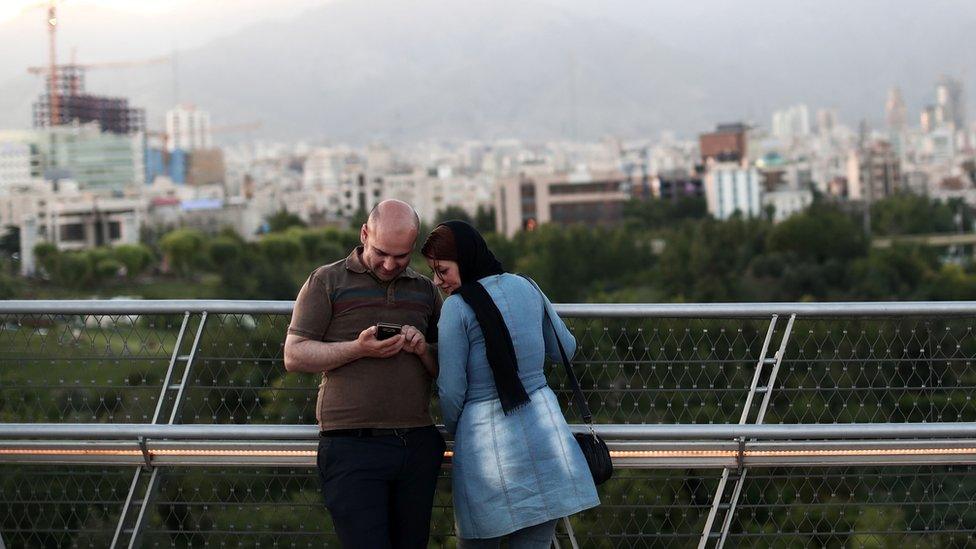 An Iranian couple look at pictures on their smartphone on the 'Nature' bridge in the capital Tehran on 2017