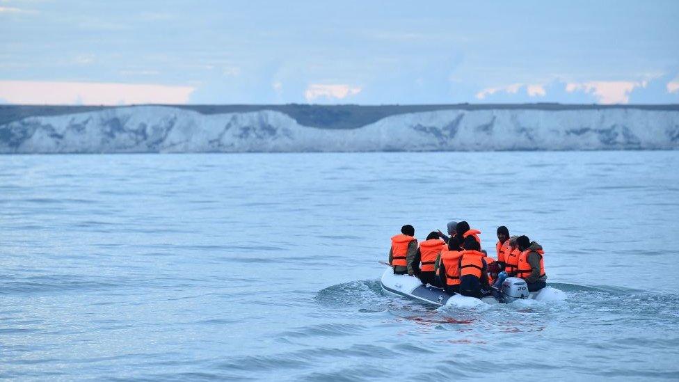 a group of migrants in a small boat look towards the cliffs of dover