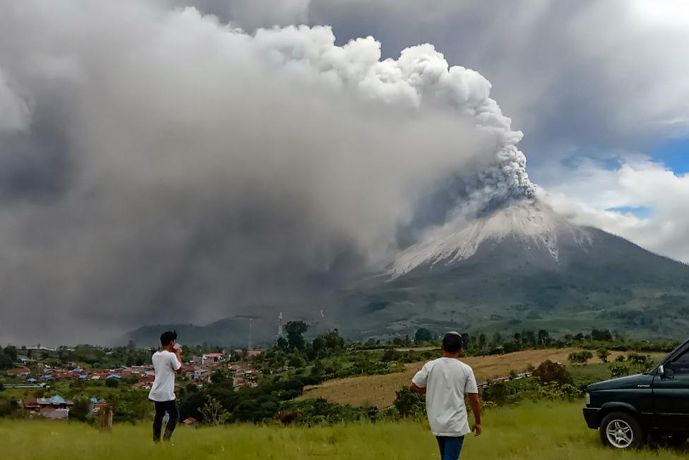 People look on as Mount Sinabung erupts spewing a massive column of smoke and ash as seen from Karo, North Sumatra, on 28 July 2021.