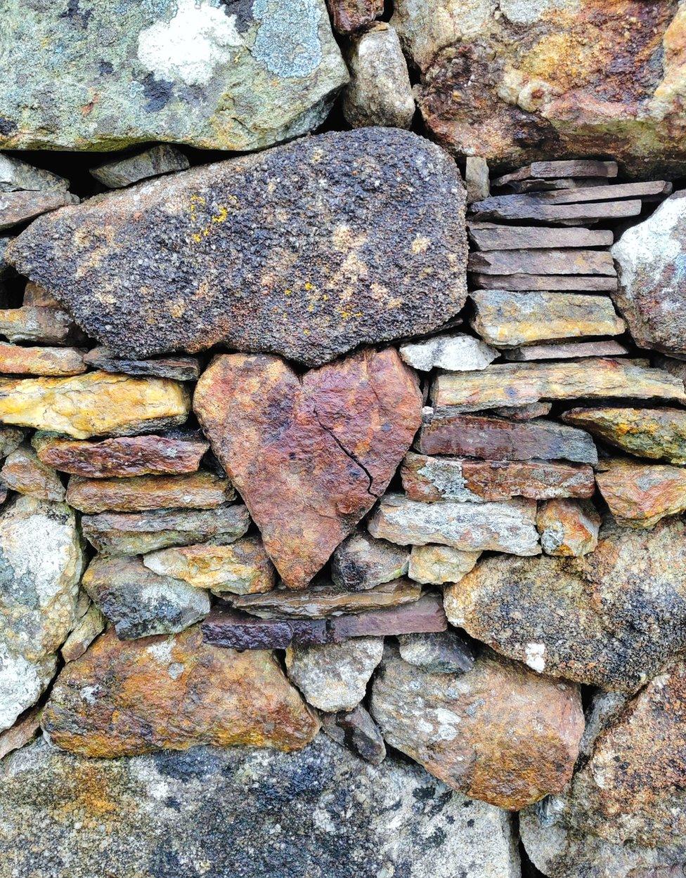 Stone wall with bricks in a variety of rough natural shapes, the centre brick shaped like a heart with a crack running through it