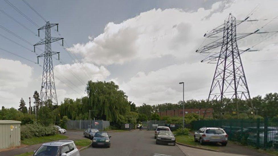 End of a road on a business park, showing grass and trees with electricity pylons