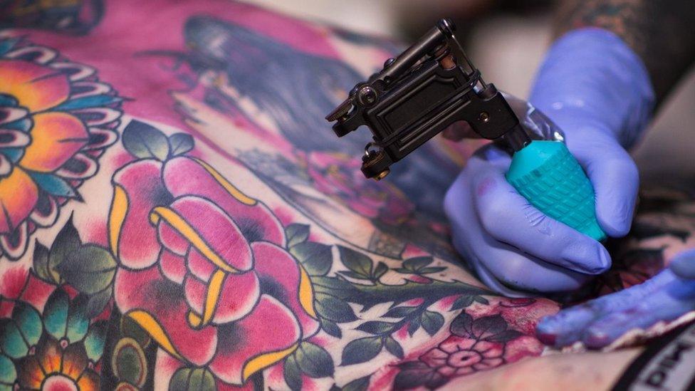 A close-up file photo from 2017 tattoo convention shoes someone having colour applied to large floral back tattoo