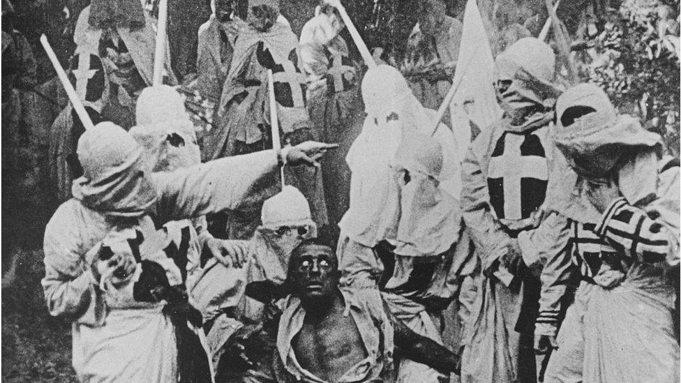 Black and white photograph of a group of Klansmen surrounding freedman Gus (played by white actor Walter Long in blackface) in a scene from Birth of Nation