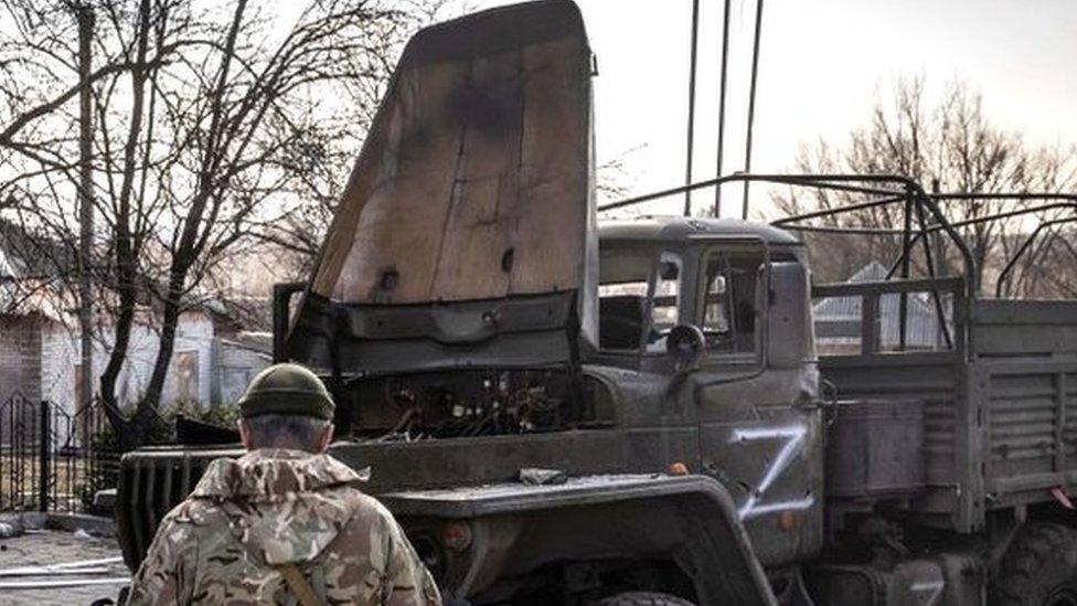 A Ukrainian serviceman stands near a Russian army truck in the north-eastern city of Trostianets