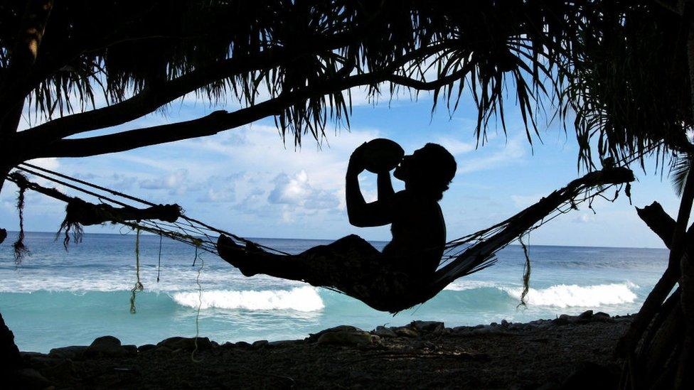 Bob Lisale drinks coconut milk as he watches the king tides pound the coast of Funafuti Atoll, 19 February 2004, home to nearly half of Tuvalu's entire population of 11,500