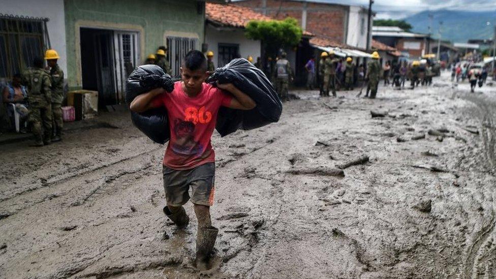 A young man carries his belongings across a muddy street, after a mudslide due to heavy rains affected Corinto in Cauca department, southwest Colombia on November 8, 2017