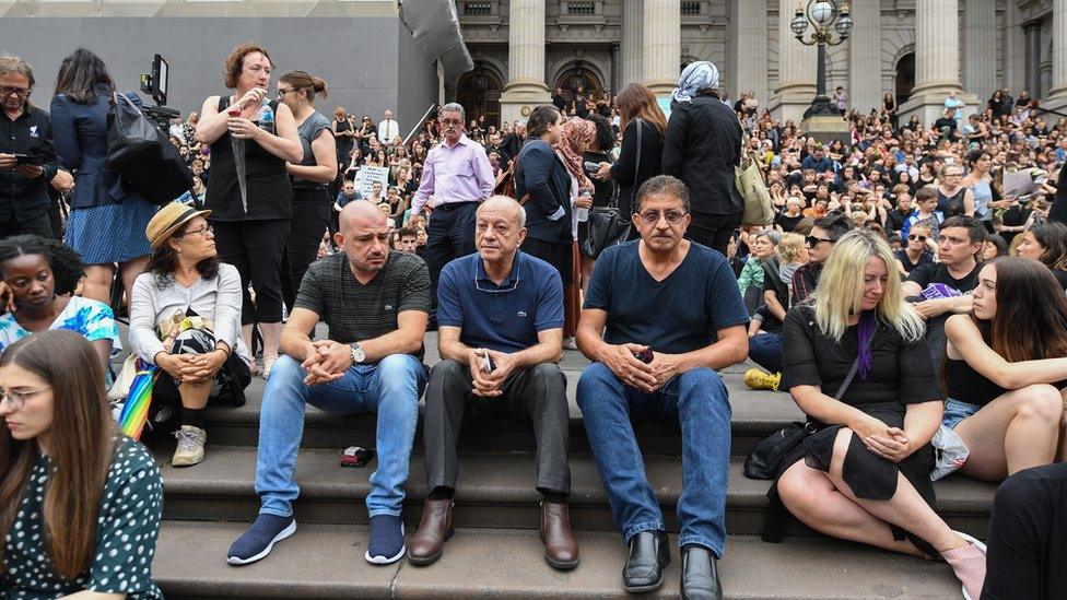 Saaed Maasarwe (centre) sitting down among a crowd of mourners at a vigil for his daughter in Melbourne