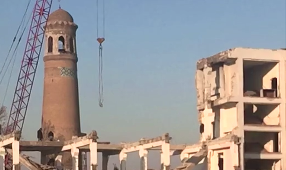 A crane and partially demolished buildings stand next to the minaret