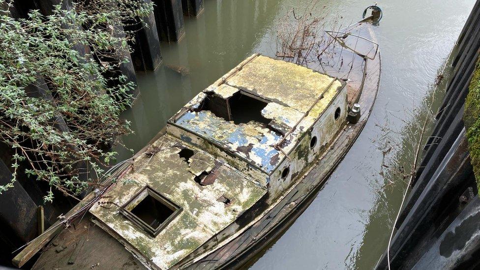 A boat slowly sinking with a broken roof and weeds growing from it