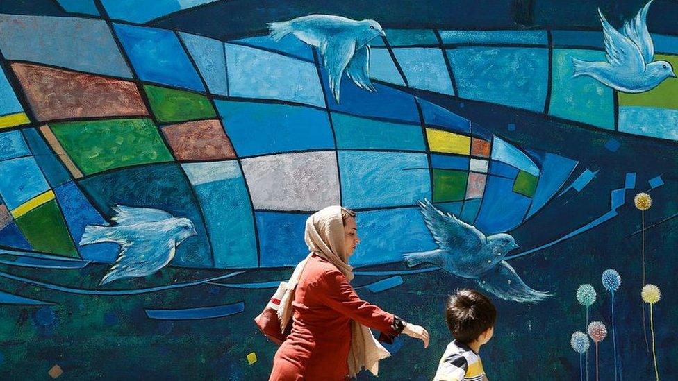 woman and child walk past mural with birds in Iran