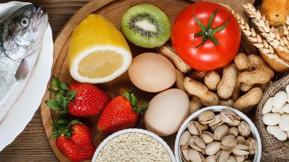 Food allergy concept. Almonds, milk, pistachios, tomato, lemon, kiwi, trout, strawberry, bread, sesame seeds, eggs, peanuts and bean on wooden table